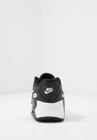 Sapatilha Nike em preto e branco com um cabedal texturizado, colarinho almofadado e logotipo proeminente no calcanhar, com um design de sola de ar distinto.