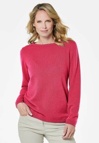 Roze lange mouwen trui in een zachte gebreide stof; heeft een ronde hals en een losse pasvorm met geribde manchetten. Gecombineerd met beige broeken.
