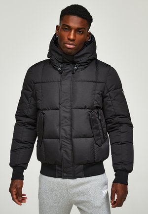 Schwarze Pufferjacke mit Kapuze, ausgestattet mit einem gesteppten Design, Reißverschlusstaschen und gerippten Bündchen. Der Stoff wirkt glatt und leicht.
