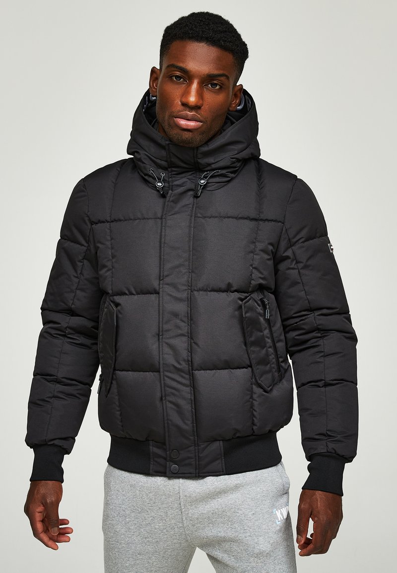 Schwarze Pufferjacke mit Kapuze, ausgestattet mit einem gesteppten Design, Reißverschlusstaschen und gerippten Bündchen. Der Stoff wirkt glatt und leicht.