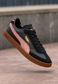 Sapatilha preta e rosa com parte superior em couro, fecho de atacadores e sola de borracha castanha. Apresenta um logótipo na lateral e detalhes texturizados.