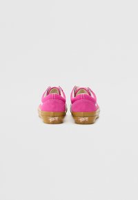 Pink suede shoes with a low-top design, rubber soles, and a rear logo accent. Features three closure loops for a secure fit.