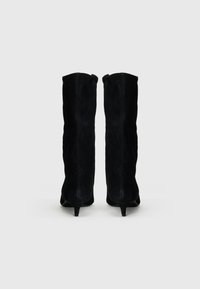 Stivali alti neri in suede con punta affusolata e tacco sottile e svasato. Texture liscia con dettagli di cucitura sottili.