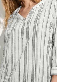 Blouse légère rayée en blanc et noir. Présente un col en V, des manches trois-quarts et des motifs verticaux à pois. Texture douce.