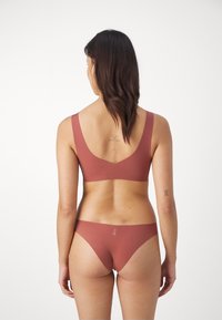 Rödbrun tvådelad lingerie-set bestående av en sömlös bralette och en kaxig bikiniunderdel med en ren design och minimal varumärkning.