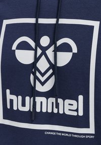 Námornícky modrá mikina s kapucňou z bavlneného zmesi so veľkým bielym logom s geometrickými tvarmi, kapucňa so šnúrkou a textom "ZMEŇTE SVET PROSTREDNÍCTVOM ŠPORTU."