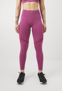 Strakke hoge taille legging in een gestructureerde dieproze stof; met subtiele donkerroze panelen. Gepaarde met zwarte sportschoenen.