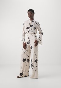 Crème blouse en wijde broek set met zwart bloemmotief, lichtgewicht stof, knoopsluiting bij de hals en ontwerp met belmouwen.