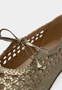 Μεταλλικό χρυσό μπαλαρέ παπούτσι με πλεκτό μοτίβο και διακοσμητικό φιόγκο στην άνω άκρη.