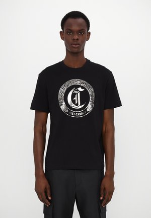 T-shirt en coton noir arborant un graphisme circulaire argenté avec une lettre « C » stylisée et un motif en peau de serpent. Manches courtes, design col rond.