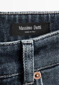 Tmavě modré denimové džíny s texturovaným povrchem, opatřené koženou štítkem s nápisem "Massimo Dutti" a "Vyrobeno v Itálii".