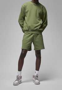Olijfgroene sweatshirt en shorts set gemaakt van zachte stof, met een ronde hals, ribbelmanchetten en een subtiel logo. Draag het met grijs-witte sneakers.