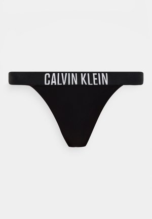 String noir Calvin Klein avec logo blanc en caractères gras sur la ceinture élastique, sur un fond blanc uni.