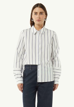 White button-up shirt featuring navy vertical stripes, long sleeves with cuffed edges, and a tailored fit. Paired with dark denim pants.