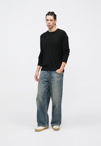 Μαύρο πουλόβερ με ριγέ υφή, άνετο μπλε τζιν παντελόνι και μπεζ αθλητικά παπούτσια. Το σύνολο έχει άνετη εφαρμογή με διακριτική υφή και καθαρό σχεδιασμό.