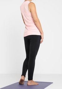 Camiseta sin mangas de color rosa claro y leggings negros. La camiseta tiene una textura suave, mientras que los leggings son ajustados y elásticos.