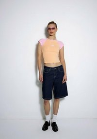 Krótki, pomarańczowy top z krótkim rękawem i różowymi akcentami oraz haftem kwiatowym; ciemnoniebieskie szorty bermudy; białe skarpety; czarne mokasyny.