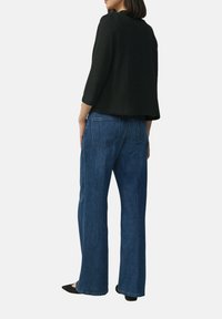 Zwart cropped trui met driekwart mouwen, gecombineerd met blauwe wijde jeans. De jeans hebben achterzakken en een klassieke denimafwerking.
