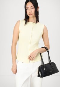 Pale yellow sleeveless top with ribbed texture and button details, paired with a black leather handbag featuring double handles and zipper.