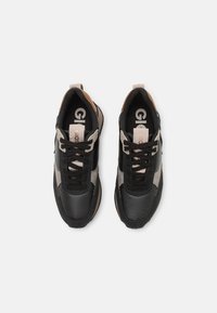 Zapatillas de cuero negro con acentos en beige y marrón claro, que cuentan con cierre de cordones, un cuello acolchado y detalles del logo en la lengüeta.