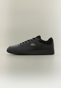 Baskets en cuir noir avec semelle en caoutchouc, bout arrondi, design à lacets et logo Lacoste vert. Détails texturés sur les côtés.