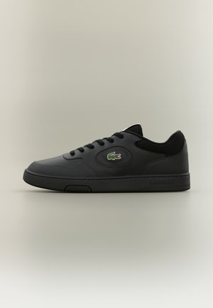Baskets en cuir noir avec semelle en caoutchouc, bout arrondi, design à lacets et logo Lacoste vert. Détails texturés sur les côtés.