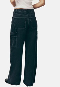 Pantaloni cargo negri cu talie înaltă, cu picioare largi, două buzunare laterale și țesătură de denim texturată. Prezintă accente de broderie pe buzunarele din spate.
