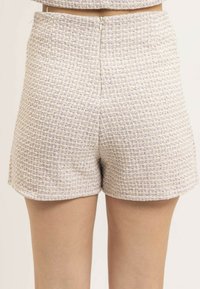 Shorts en tissu tissé de couleur beige clair avec des accents violets, présentant un motif texturé, une taille haute et une fermeture éclair centrée à l'arrière.