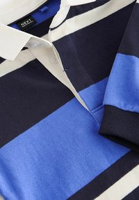 Navy en blauw gestreept poloshirt van zachte stof. Beschikt over een witte kraag, knoopsluiting en een geribbelde manchet op de mouw.