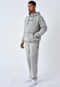 Grijze katoenen hoodie en joggingbroek set, met een kangoeroezak, contrasterende stiksels en geribbelde boorden. Draag het met witte sneakers.