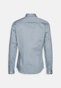 Vaaleansininen pitkähihainen napitettava paita näkyy takaapäin, klassisella kauluksella ja napitetuilla hihoilla.