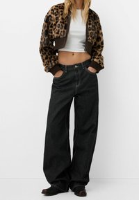 Giacca corta con stampa leopardata, con polsini e orlo a coste marroni, abbinata a jeans a vita alta neri con gamba ampia e cuciture in contrasto.