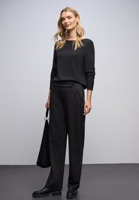 Pull noir à manches longues, ajusté aux poignets ; pantalon noir taille haute, large avec une texture subtile ; sac à main noir ; bottines noires.