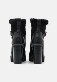 Černé kotníkové boty na podpatku s umělou kožešinou, vyrobené z kůže a semiše, vybavené bočním zipem a dekorativními detaily.