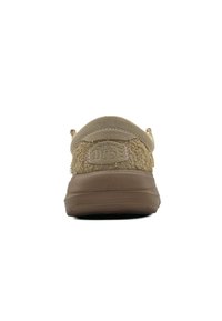 Zapato de ante color marrón claro con un upper texturizado y suave, diseñado con una forma redondeada y una suela gruesa de goma marrón. La parte trasera presenta un parche con el logo.