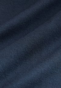 Dunkelblauer Stoff mit feiner gerippter Textur, in Nahaufnahme gezeigt, mit sanften Falten und weichem Licht.