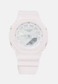 Montre G-SHOCK avec un bracelet en résine rose clair, cadran rond blanc, affichage analogique et numérique, étanche jusqu'à 20 bars, et accents en métal.