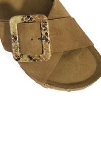 Sandale en daim marron avec un design ouvert à l'avant et une grande boucle carrée au motif serpent. Semelle intérieure texturée pour le confort.