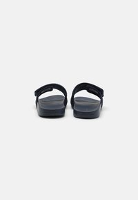 Tengerészkék flip-flop szandál, textúrált pánttal és párnázott talppal. Minimalista dizájnnal és a márka logójával az egyik oldalon. Tartós anyagból készült.