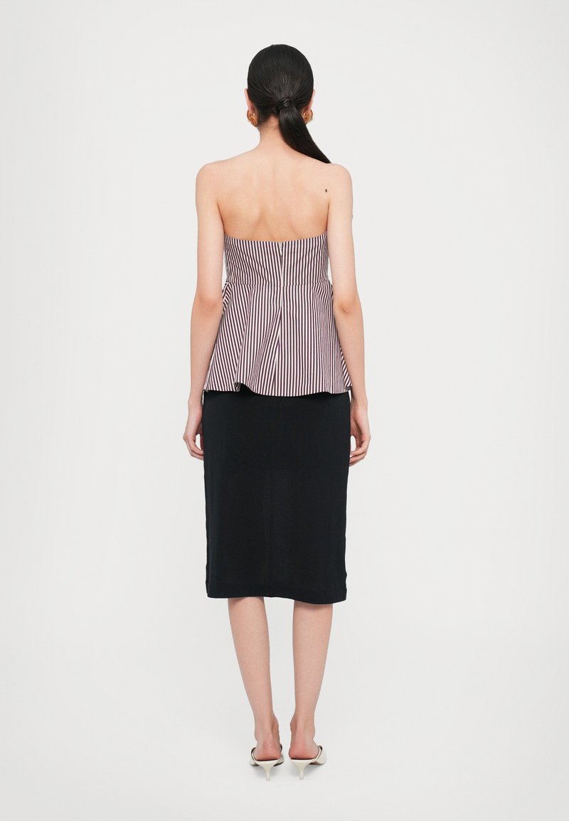 Axellös peplum-top med vertikala lila och vita ränder, kombinerad med en figurnära svart kjol. Slät tyg med en strukturerad design.