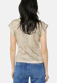 Top a maniche corte in beige metallico con un motivo a stampa leopardata. Presenta una vestibilità morbida e un tessuto leggermente testurizzato.