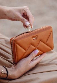 Tan leather wallet with a quilted design, featuring a golden zipper and a branded zipper tag. Handheld, showcasing a smooth texture.