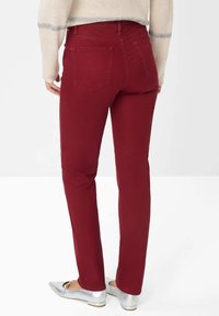 Burgunderfarbene Jeans mit geradem Bein, die zwei Gesäßtaschen und eine glatte Textur aufweisen, kombiniert mit silbernen Ballerinas.