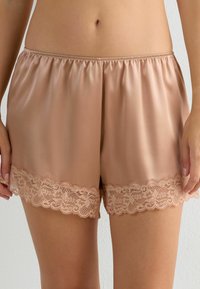 Satin shorts i ljusbeige färg med dekorativ spetsdetalj vid fållen. Elastisk midja ger en bekväm passform.