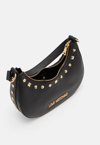 Svart läderhandväska med guldnitar, dragkedjor och en logotyp. Strukturerad design med en böjd form och ett enda axelband.