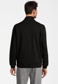 Giacca nera a maniche lunghe con una texture morbida, dotata di colletto rialzato e polsini a costine, progettata per una vestibilità rilassata.