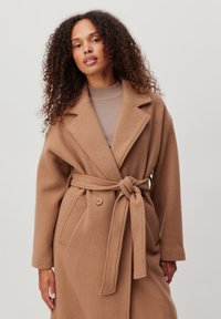 Tan wollen blend jas met een sjaalkraag, een strikceintuur en dubbele knoopsluiting. Textuurstof; lange mouwen en zijzakken.