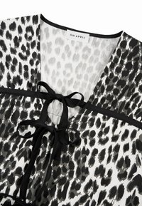 Svart-hvitt leopardmønstret bluse med V-hals, med en sentral sløyfedetalj og kontrasterende svarte kanter. Lett stoff.