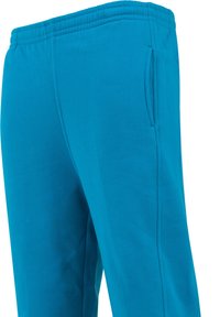 Pantaloni de trening turcoaz cu o talie elastică, buzunare laterale și o textură netedă din bumbac, având o croială relaxată.
