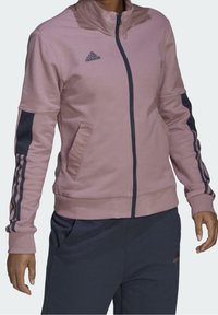 Roze jas met ritssluiting, met marineblauwe accenten en drie strepen op de mouwen. Voorzien van zijzakken en geribde manchetten voor een aansluitende pasvorm.